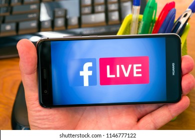 PIATRA NEAMT, ROMANIA - JULY 30, 2018: Hand holds a mobile phone with Facebook Live logo on the scrren, office background.
