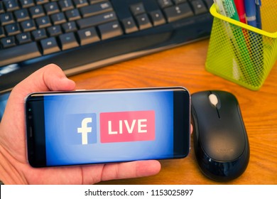 PIATRA NEAMT, ROMANIA - JULY 30, 2018: Hand holds a Samsung S8+ with Facebook Live logo on the screen, office background.