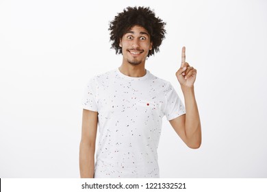 Pick me. Portrait of active and excited handsome male with funny expression and curly hairstyle raising index finger in one gesture, smiling broadly and staring thrilled with popped eyes at camera