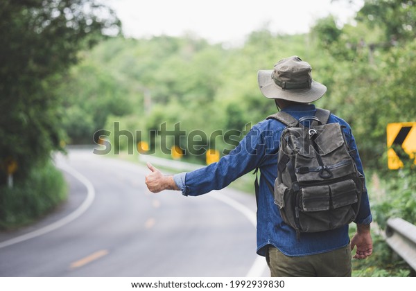 Pick me up. Man hitchhiking on the side of the\
road. Man try stop car thumb up. Hitchhiking one of cheapest ways\
traveling.