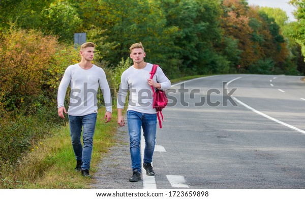 Pick spot where car can easily pull aside. Men\
backpack walking road. Twins walk along road. Adventure concept.\
Guys hitchhiking on road. Tourist traveler travel auto stop.\
Transporting issues.