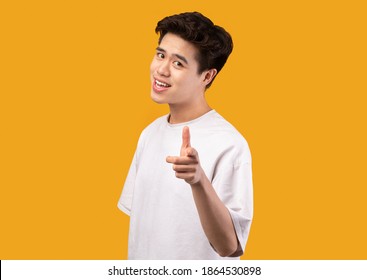 I Pick You. Portrait Of Casual Asian Guy In White T-shirt Pointing Finger At Camera, Posing Isolated Over Orange Studio Background Wall. Positive Smiling Man Choosing And Indicating