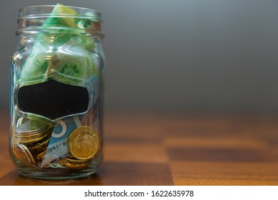 Pickering, Ontario/Canada - January 16 2020: Transparent Glass Jar With Money Inside On Top Of Wooden Table.  Concept For Swear Jar, Savings, Budgeting, Trip Fund.