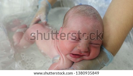 Newborn in the bathtub with her mother washing her hair