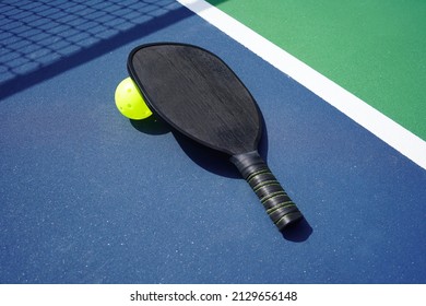 Pickle Ball Paddle And Pickle Ball On Court With Net Shadow In Background.