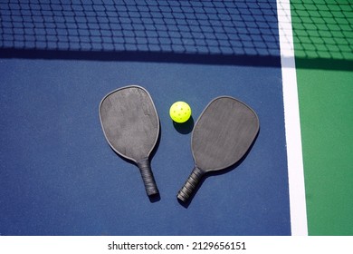 Pickle Ball Paddle And Pickle Ball On Court With Net Shadow In Background.