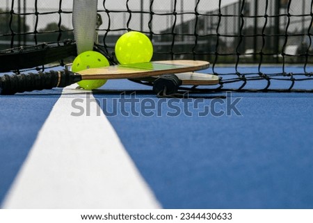 Pickleball paddles and two yellow whiffle balls on a blue court on a white line close up.