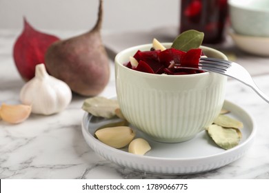 Pickled beets with garlic in bowl on white marble table