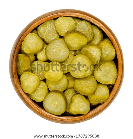 Pickled cucumber discs, also known as pickle or gherkin, in wooden bowl. Small pickled cucumbers with bumpy skin, sliced. Baby pickles. Close-up from above, over white, isolated macro food photo. Foto stock © 