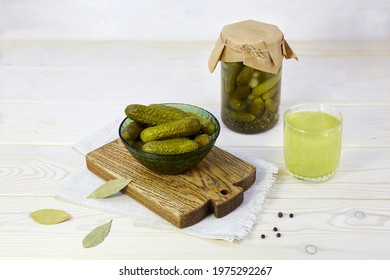 Pickled Cucumbers In A Bowl And Jar, Pickle Juice In Glass On A White Wooden Background. Homemade Marinated Gherkins. 