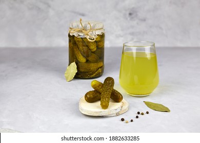 Pickled Cucumbers In A Glass Jar And Pickle Juice In Glass On A Light Background. Homemade Fermented Or Marinated Cucumbers. Healthy Energy Drink For Athletes.