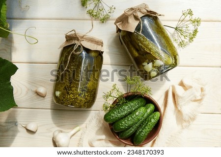 Pickled cucumbers in jars, fresh cucumbers on bowl, dill, garlic on a white wooden background. Home canning. Top view.