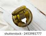 Pickled cucumbers on a fork and in a jar on a wooden background. 