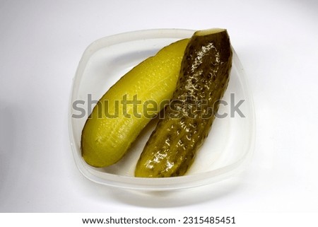 Pickled cucumbers in a plastic container on a white background.