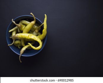 Pickled green chili peppers in blue bowl isolated on black background