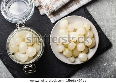 Pickled mini baby onions in jar and plate on kitchen table. Top view.