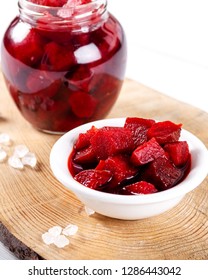 Pickled red beetroot in bowl and jar on wooden background.