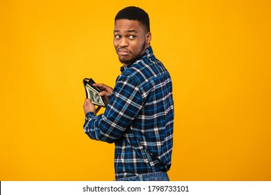 Pickpocketing. Sneaky Black Man Holding Wallet With Cash Money Standing On Yellow Background. Studio Shot