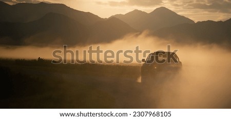 Pickup truck car drive fast at the country road with clouds of dust and beautiful mountains at the background. Sunrise in valley with a steam. Panoramic view with free space for text