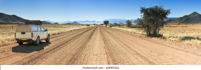 Pickup Truck Driving On Long Straight Desert Road Towards Mountains.