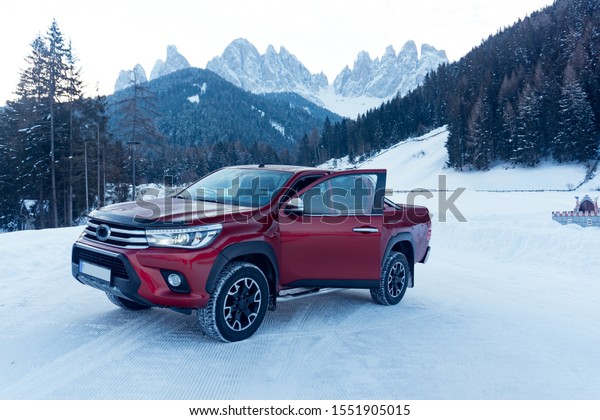 \
Pickup truck on road, Beautiful winter road under\
snow mountains Dolomites, Italy. Shiny red truck measuring the\
depth of the snow
