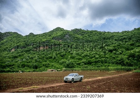 The pickup truck is parked in newly glown flield.Front of The moutain. valley of Thailand. a newly planted field