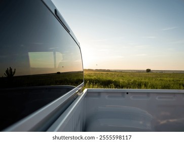 Pickup truck rear window. Looking at the green meadow in the background from the cargo bed of white pickup truck.