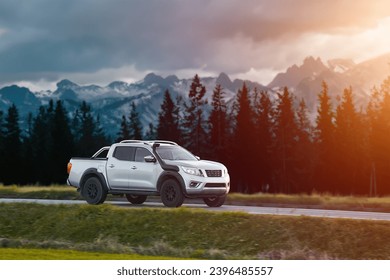 Pickup truck running on the beautiful road along the mountains and forest. Front side view of a pickup truck with a snorkel on a highway road and majestic nature in the background.