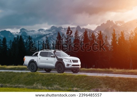 Pickup truck running on the beautiful road along the mountains and forest. Front side view of a pickup truck with a snorkel on a highway road and majestic nature in the background.