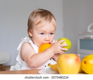 Picky Eater Blond Blue-eyed Toddler Sitting At Table, Holding And Biting Colorful Fresh Fruits From Plate. Healthy Children Eating Habits. Snack Break For Babies. Vitamin Vegetarian Food.