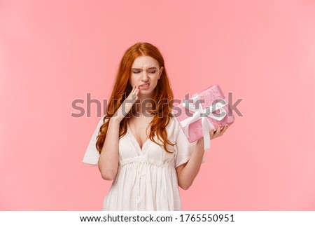 Picky and ignorant displeased spoilt redhead girl, holding wrapped cute box with gift, looking with scorn and disappointment at present, grimacing, cringe displeased, dislike it