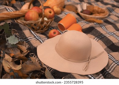 Picnic in autumn park. Checkered plaid with felt hat, coffee cups, wicker baskets with apples, pumpkins and croissants. Autumn inspiration with no people. - Powered by Shutterstock