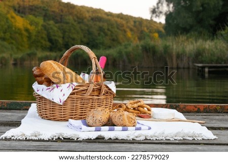 Picnic basket near a beautiful lake with wine and blanket. Relaxing image of an outdoor picnic setup