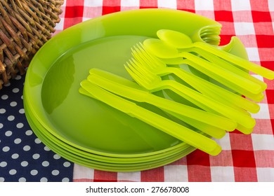 Picnic Basket And Plastic Dishes On Red, White And Blue Tablecloth Indicative Of The American Flag.  Traditional July 4th Picnic Scene.