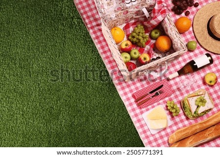 Picnic basket with tableware, different snacks, wine and hat on green grass outdoors, top view. Space for text