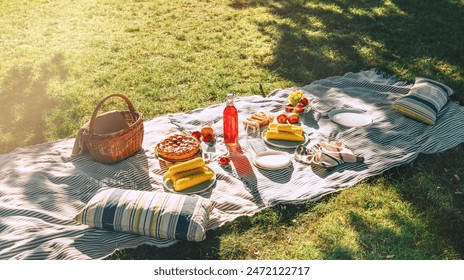 Picnic blanket with boiled corn, fruits, just backed pie, a bottle of juice, basket still life in the city summer park. No people. - Powered by Shutterstock