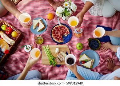 Picnic blanket with healthy food and human hands with drinks over it - Powered by Shutterstock