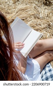 Picnic In Countryside. Young Woman In White Dress Sitting On Haystack In Harvested Field, Reading Blank Book. Book Mockup