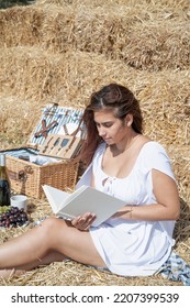 Picnic In Countryside. Young Woman In White Dress Sitting On Haystack In Harvested Field, Reading Blank Book. Book Mockup