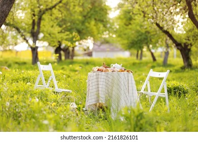 picnic with decorated table with croissants, fruits and drinks in beautiful blossom spring green park, romantic date table food setting for two.