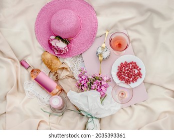 Picknick-Wohnung lag auf beiger Decke mit rosafarbenem Strohhut, Baguette, Flasche Roswein, Kerzen, Blumenstrauß, köstliche Käse und schöne Brille . Draufsicht. ästhetisches Picknick-Konzept