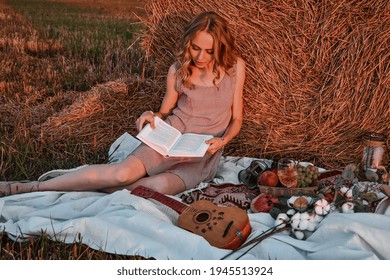 Picnic at the hayloft. Woman sitting near a straw balereading book. Summer, beauty, fashion, glamour, lifestyle concept. Cottagecore farmcore naturecore. Pastoral life
