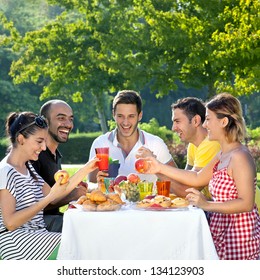 Picnic. Multi Ethnic Friends Sharing An Enjoyable Meal Seated At A Table Outdoors In The Garden Laughing And Joking Together