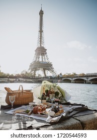 Picnic near the Seine in front of Eiffel tower. Fruits, french cheeses, shrimps, snacks, croissants, oysters, foie gras, delicacies, a bouquet of flowers and a bottle of expensive champagne.