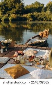 Picnic On A Wooden Jetty Near The Water. A Decorated Picnic Area Awaiting Guests. Cheese And Fruit Plate On A Picnic Table. Evening Picnic Party With Golden Sunlight.