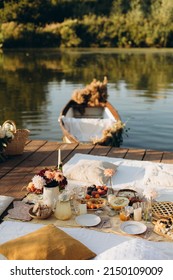 Picnic On A Wooden Jetty Near The Water. A Decorated Picnic Area Awaiting Guests. Cheese And Fruit Plate On A Picnic Table. Evening Picnic Party With Golden Sunlight.