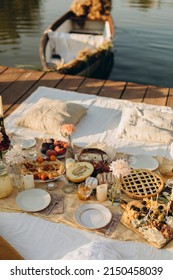 Picnic On A Wooden Jetty Near The Water. A Decorated Picnic Area Awaiting Guests. Cheese And Fruit Plate On A Picnic Table. Evening Picnic Party With Golden Sunlight.