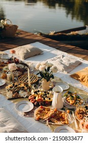 Picnic On A Wooden Jetty Near The Water. A Decorated Picnic Area Awaiting Guests. Cheese And Fruit Plate On A Picnic Table. Evening Picnic Party With Golden Sunlight.