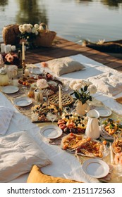 Picnic On A Wooden Jetty Near The Water. A Decorated Picnic Area Awaiting Guests. Cheese And Fruit Plate On A Picnic Table. Evening Picnic Party With Golden Sunlight.