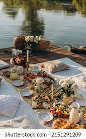 Picnic On A Wooden Jetty Near The Water. A Decorated Picnic Area Awaiting Guests. Cheese And Fruit Plate On A Picnic Table. Evening Picnic Party With Golden Sunlight.